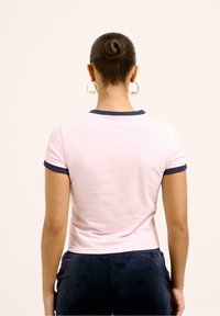Růžové tričko s přiléhavým střihem, krátkým rukávem a tmavě modrým lemem kolem výstřihu a na manžetách. Hladká bavlněná textura.