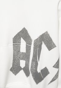 Sweat-shirt blanc avec un grand motif noir texturé à l'avant, poche kangourou et poignets côtelés.