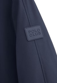 Manica di giacca blu navy con un tessuto testurizzato, caratterizzata da un'etichetta rettangolare blu scuro "POLO CLUB" cucita sulla spalla.