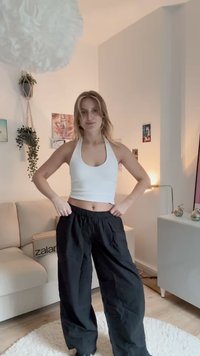 Bijela halter crop top kombinirana s crnim, širokim hlačama. Glatka tkanina i elastičan pojas, smješteno u prostoriji s blagim osvjetljenjem.