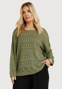 Olivgrön stickad tröja med en öppen vävstruktur med horisontella och vertikala linjer, långa ärmar och avslappnad passform.