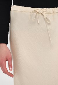Light beige skirt with a wrinkled texture, featuring an elastic waistband and a tie closure at the top. Simple design and smooth fabric.