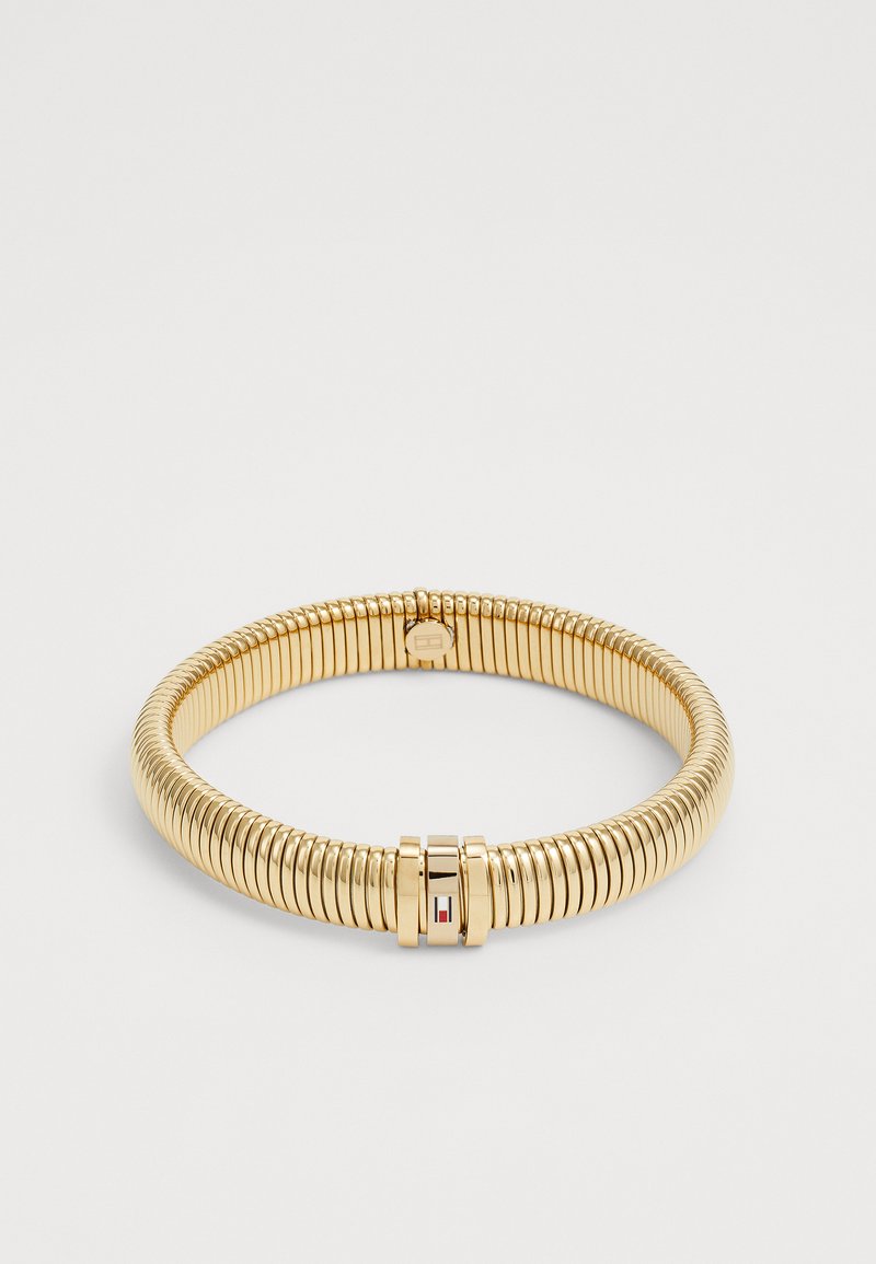 Bracciale in metallo color oro, composto da anelli circolari, con un design liscio e flessibile. Presenta un piccolo logo come dettaglio nell'area della chiusura.