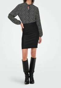 Zwart-wit gebloemde blouse met lange mouwen en een sleutelgat in de halslijn, gecombineerd met een aansluitende zwarte rok en zwarte kniehoge laarzen.