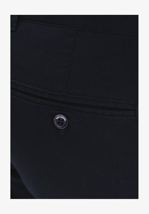 Czarne dżinsy mają tylną kieszeń z poziomym rozcięciem, ozdobioną okrągłym czarnym guzikiem z wytłoczonym napisem.