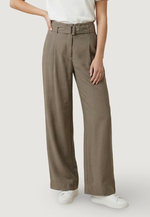 Donna che indossa pantaloni verde oliva a vita alta e gamba larga con cintura, sneaker bianche e top bianco a maniche corte infilato dentro.