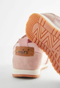 Rosa sneakers med en blandning av mocka och tyg, med en texturerad gummisula som visar ett zigzag-mönster och en brun etikett med texten "mini."