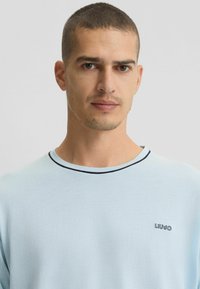 T-shirt di cotone azzurro chiaro con colletto rotondo, rifiniture nere in contrasto e un piccolo logo sul petto. Tessuto morbido e vestibilità comoda.