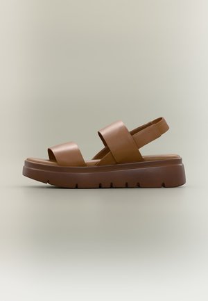 Brun plateau-sandal med to brede stropper og en slingback-strop, med en kraftig sål med mønster for ekstra greb.