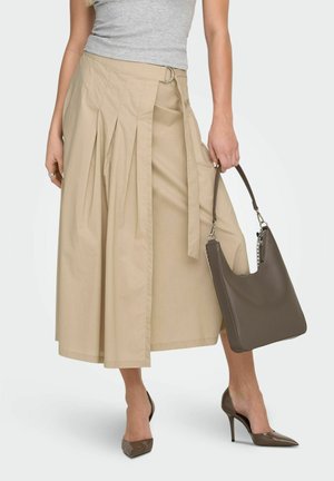 Femme portant une jupe midi plissée beige, un débardeur gris, des talons pointus marron, tenant un sac à main en cuir marron sur le côté.