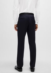 Marineblaue formelle Hosen mit glatter Textur, flachem Vorderteil und seitlichen Taschen. Kombiniert mit einem weißen Hemd und einem schwarzen Gürtel, in taillierter Passform.
