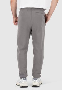 Grijze sweatpants gemaakt van zacht materiaal, met een recht gesneden ontwerp, elastische tailleband en een achterzak. Gecombineerd met witte sneakers.