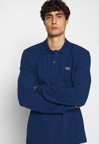 Marineblaue Langarm-Polohemd mit klassischem Kragen und einem dezenten, gestickten Krokodil-Logo auf der linken Brust. Strukturierter Stoff.