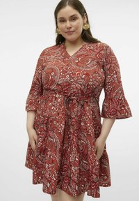 Robe rouge à motifs paisley avec des manches cloche trois quarts, une taille cintrée et des poches. Présente des motifs floraux blancs et paisley intriqués.
