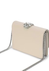 Bolso de mano de cuero beige con un cierre adornado con cristales y cadena plateada. Forma rectangular, textura suave y diseño minimalista.