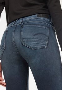 Jeans de mezclilla azul oscuro con un diseño ajustado, que cuentan con dos bolsillos traseros, sutiles detalles de costura y una textura suave.