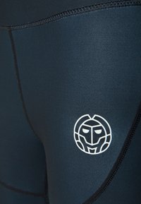 Leggings elasticizzati blu navy realizzati in materiale liscio, con cuciture piatte e un logo bianco sulla coscia.