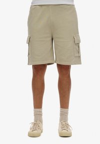 Beige cargoshorts met twee zijzakken, gestikte details en een losse pasvorm. Het materiaal lijkt zacht met een textuurafwerking.