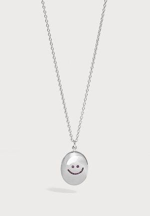 Collar con colgante de plata con un charm ovalado que presenta una pequeña cara sonriente hecha de piedras preciosas moradas en una cadena de plata.