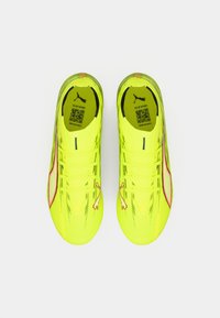 Jasnożółte buty sportowe z teksturowaną syntetyczną cholewką, z różowymi akcentami, sznurówkami oraz małym logo po boku.