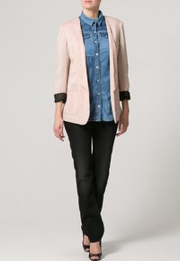 Blazer rosa claro con ribetes negros sobre una camisa de mezclilla azul, combinado con pantalones negros y zapatos de tacón negros. Diseño simple y moderno.