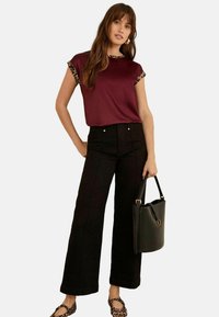 Top bordeaux a maniche corte con dettagli in stampa leopardata, abbinato a pantaloni neri a vita alta e a gamba larga e una borsa nera. Scarpe basse in tessuto.