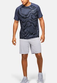 Granatowa sportowa koszulka z czarnym falistym wzorem, krótkie rękawy, okrągły dekolt, w połączeniu z jasnoszarymi szortami; wykonana z oddychającej tkaniny.