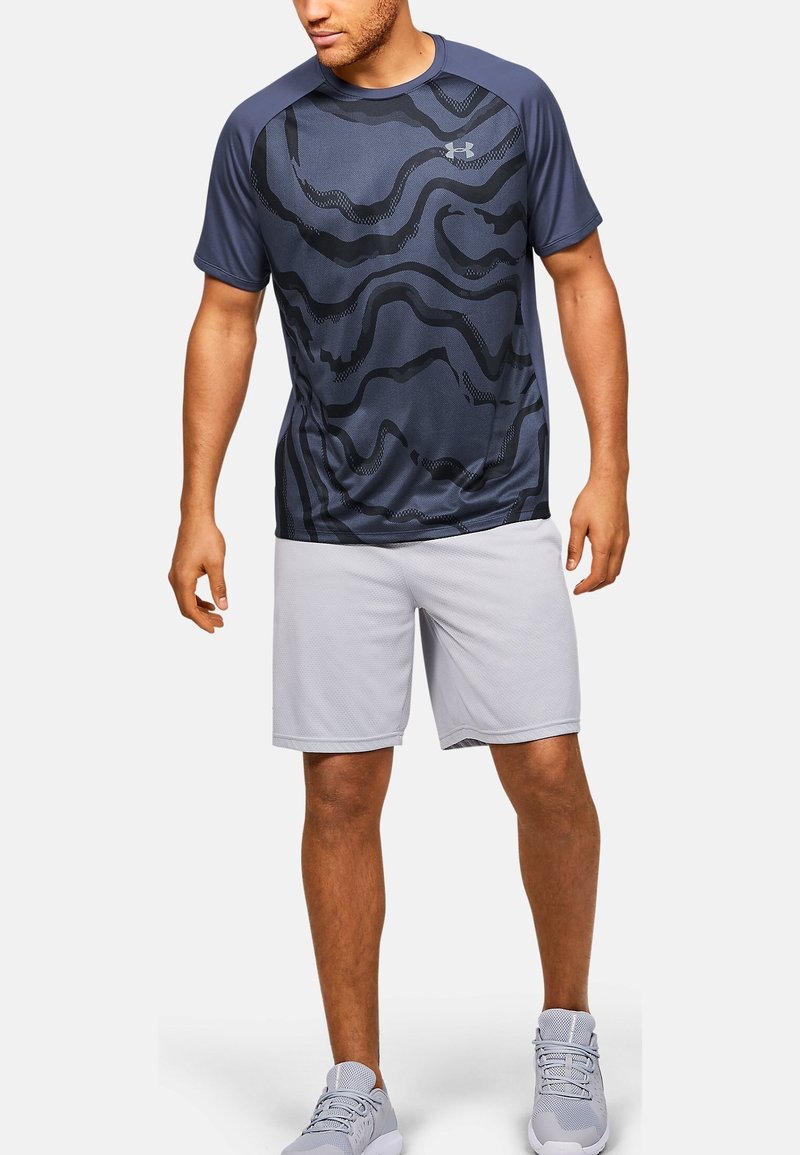 Granatowa sportowa koszulka z czarnym falistym wzorem, krótkie rękawy, okrągły dekolt, w połączeniu z jasnoszarymi szortami; wykonana z oddychającej tkaniny.