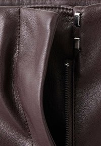 Braune Lederhandtasche mit strukturiertem Finish, ausgestattet mit einem Reißverschluss und Metallakzenten. Das Innere ist sichtbar und zeigt Nähdetails.