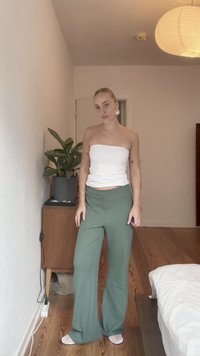 Biely top bez ramienok a zelené široké nohavice s textúrovaným vzorom. Model pózuje proti minimalistickému interiéru s drevenou podlahou.