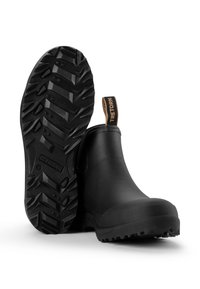 Schwarze Gummistiefel mit einem strukturierten Sohlenprofil, ausgestattet mit einer beigefarbenen Ziehschlaufe mit dem Aufdruck "Tretorn" und einem runden Zehenbereich.