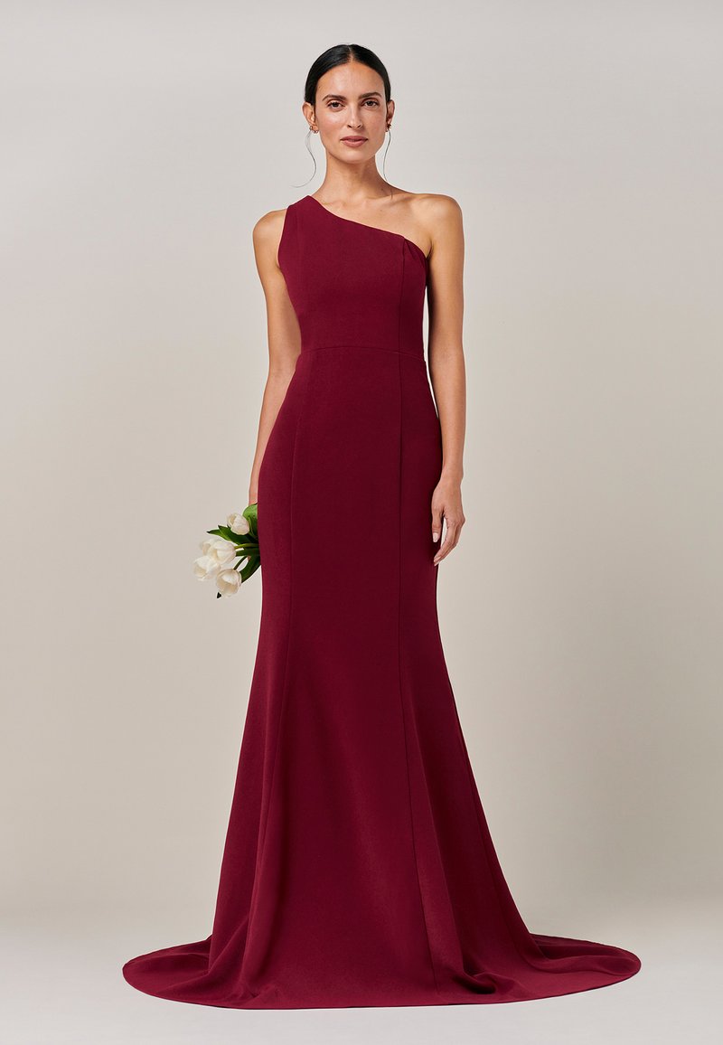 Burgundia ühe õlaga õhtukleit, millel on kehale istuv siluett ja lehviv ääris. Modell hoiab valgete tulpide kimbu. Sile kangapind.