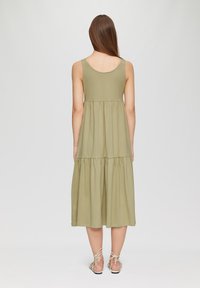 Robe maxi sans manches vert olive, présente un design en tiers avec une forme fluide et une texture douce, complétée par des sandales à lanières.