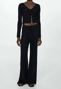 Conjunto de dos piezas de punto negro que incluye un top corto de manga larga con un lazo en la parte delantera y pantalones de tiro alto con cintura ajustable.