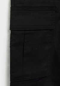 Pantalons cargo noirs en tissu de coton résistant, dotés d'une grande poche latérale et de détails de couture visibles. Le design est simple et fonctionnel.
