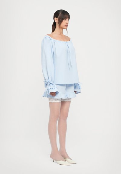Light blue off-the-shoulder top with tied sleeves and ruffled hem, paired with matching shorts featuring lace trim and white tights.