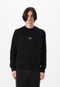 Black sweatshirt with a crew neckline, ribbed cuffs, and hem. Features white logo text on the chest. Soft cotton blend material.
