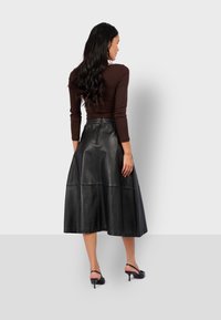 Gonna midi in pelle nera con design svasato, caratterizzata da una vita arricciata e pannelli senza cuciture. Abbinata a un top aderente marrone a maniche lunghe.