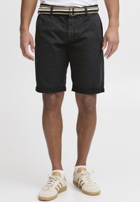 Black denim shorts with rolled cuffs, featuring side pockets and a textured belt with yellow and black stripes. Worn with light sneakers.