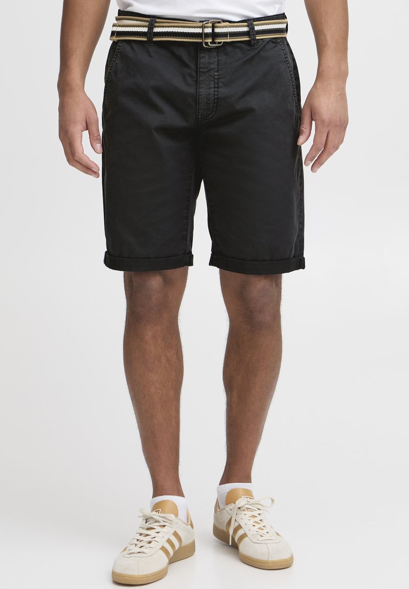 Black denim shorts with rolled cuffs, featuring side pockets and a textured belt with yellow and black stripes. Worn with light sneakers.