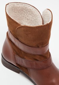 Bottine en cuir marron et daim avec deux brides horizontales et une doublure en laine blanche et moelleuse visible en haut.