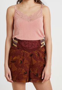 Camisole en satin rose avec des bordures en dentelle, associé à un short bordeaux présentant des motifs texturés et des accents décoratifs à la taille.