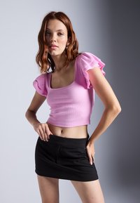 Light pink ribbed crop top with puff sleeves, paired with a black mini skirt. The top features a square neckline and smooth texture.