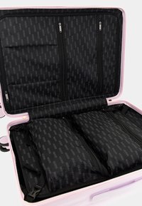 Valigia rigida rosa con interno in tessuto nero, dotata di più scomparti con zip e motivo branded. Texture liscia e design robusto.