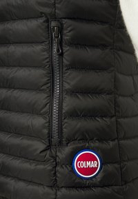 Svart vadderad väst med en ficka med dragkedja. Har horisontell quiltning och en rund, flerfärgad logotyp med texten "COLMAR".