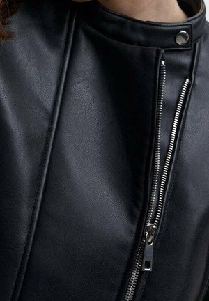 Nærbillede af en sort læderjakke med en lodret sølv lynlås og knaplukket krave på en person.