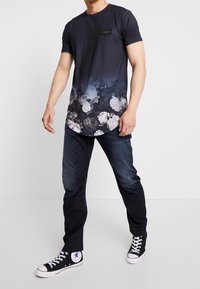 Kortärmad marinblå t-shirt med blommönster nederst, kompletterad med en liten svart bröstficka och rundad fåll.