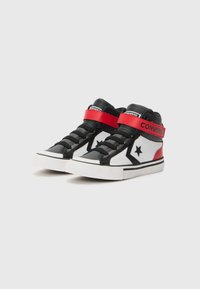 Nilkkapituiset lenkkitossut, joissa mustaa, punaista ja valkoista keinomateriaalia, velcro-tarrakiinnitys ja pyöreä varvasmuotoilu. Musta tähti-logo yksityiskohtana.