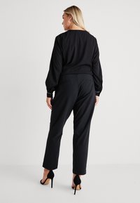 Černá blůza s dlouhým rukávem a nabíranými rukávy, zkombinovaná s černými vypasovanými kalhotami. Tento outfit se vyznačuje elegantním designem a jemnými detaily.