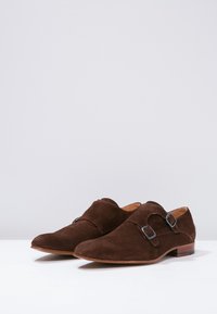 Scarpe in suede marrone con un design a doppia fibbia monk, punta tondeggiante e tacco in legno piccolo. Le fibbie sono accentuate da fibbie in argento.
